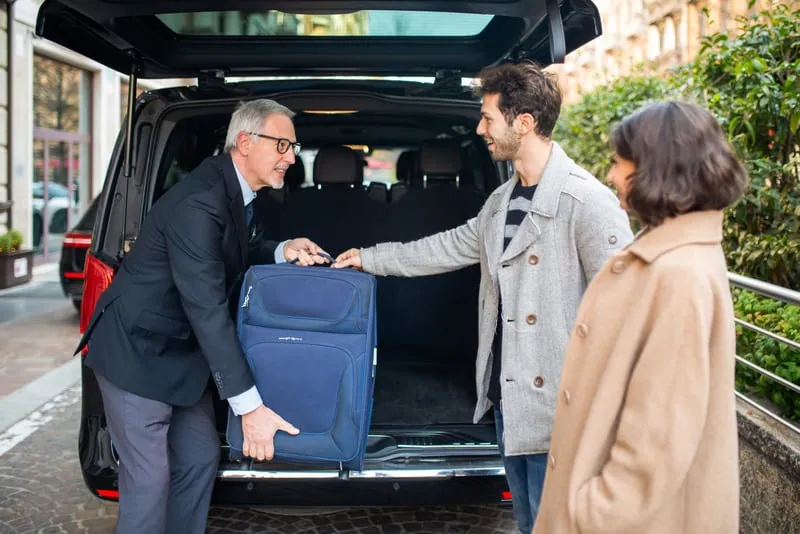 A driver loading a traveler's suitcase into a van