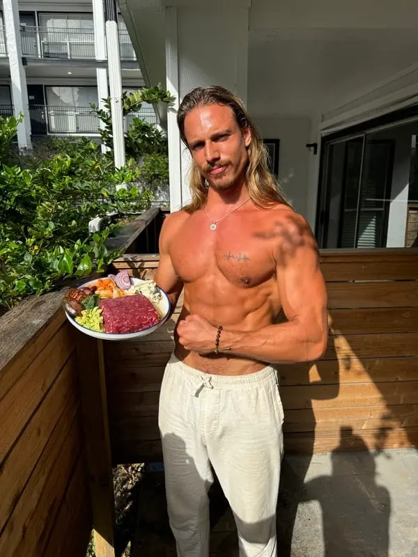 Christian Van Camp holding a plate of raw meat, fruit and vegetables on a sunny balcony