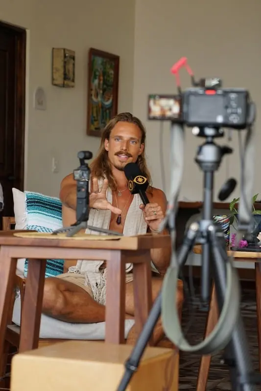 A host filming at a desk with a camera on a tripod
