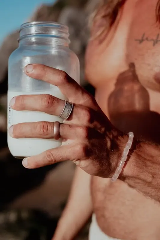 A hand holding a glass jar of raw milk