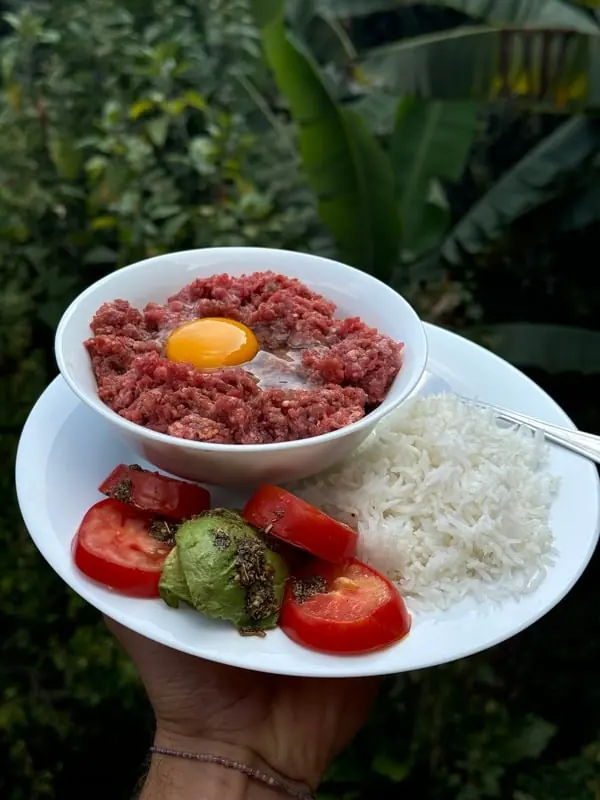 A plate of raw ground meat with an egg yolk, rice, tomatoes and avocado