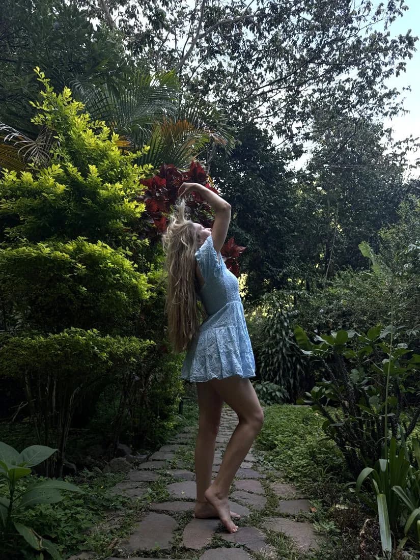 A woman in a blue dress lifting her hair on a stone path in the garden