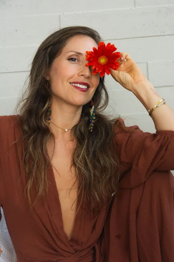 Monika Arenas smiling, holding a red gerbera daisy over one eye
