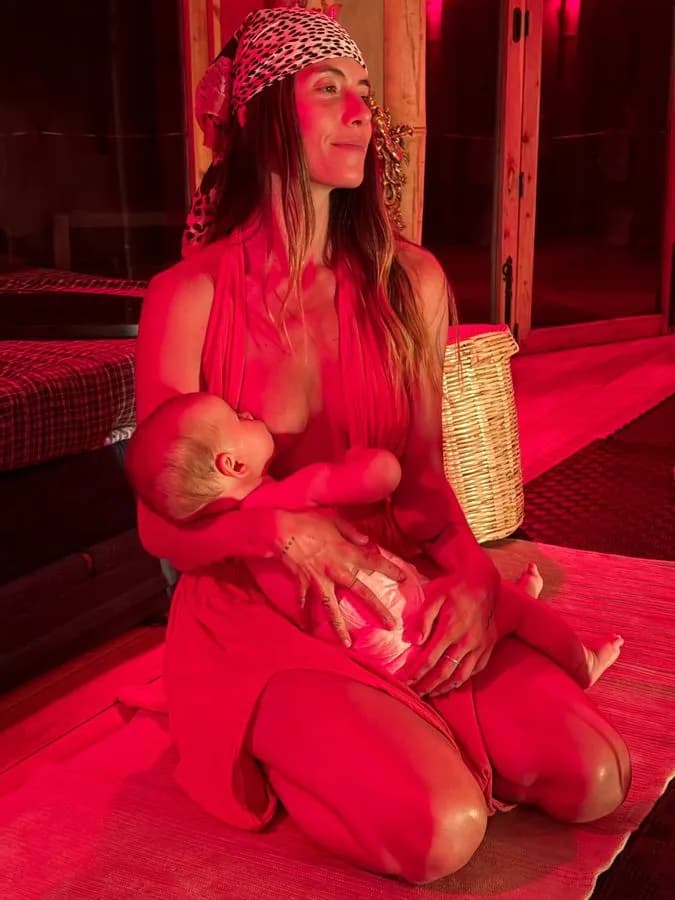 Sedona Holzinger in red light, smiling softly while nursing her baby