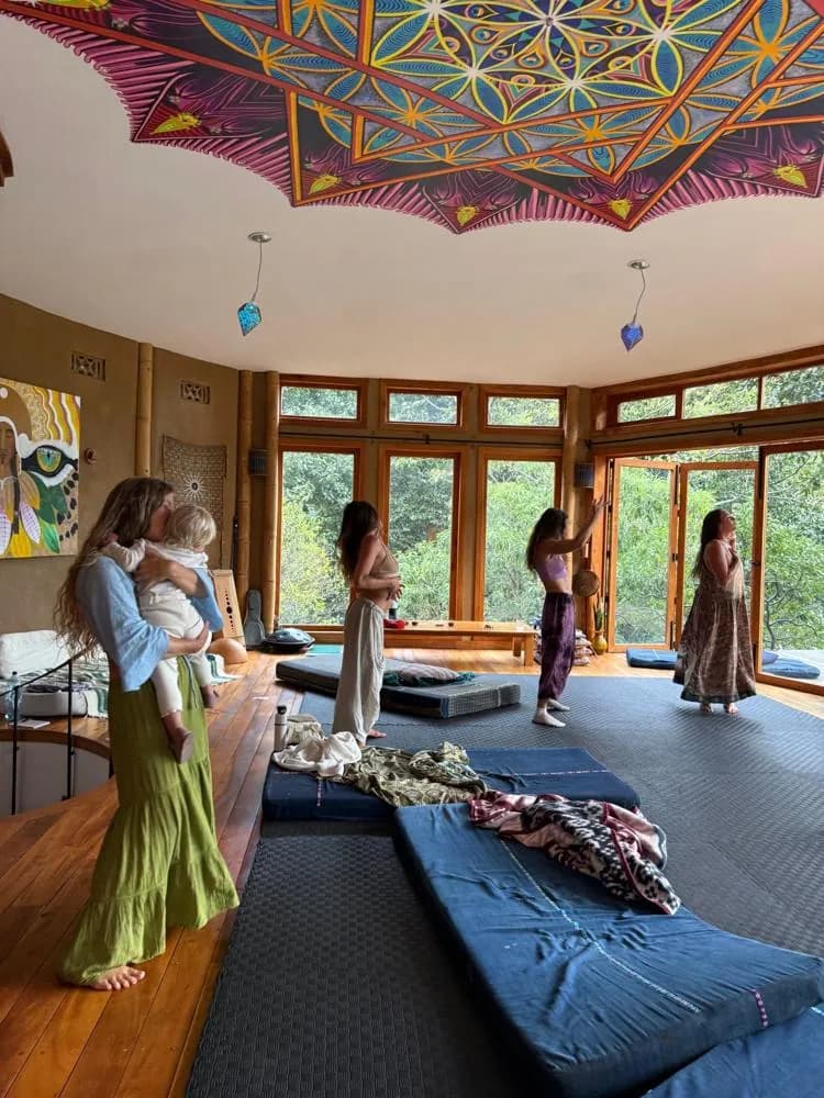 Women standing and dancing in a wood and glass studio beneath a painted mandala ceiling