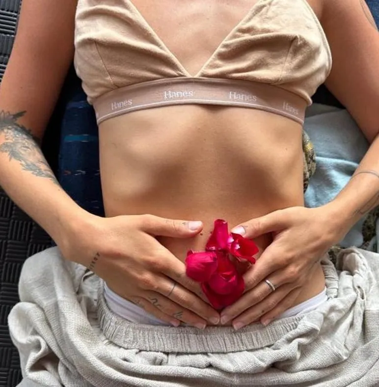 A woman lying down with her hands over her belly, holding red rose petals