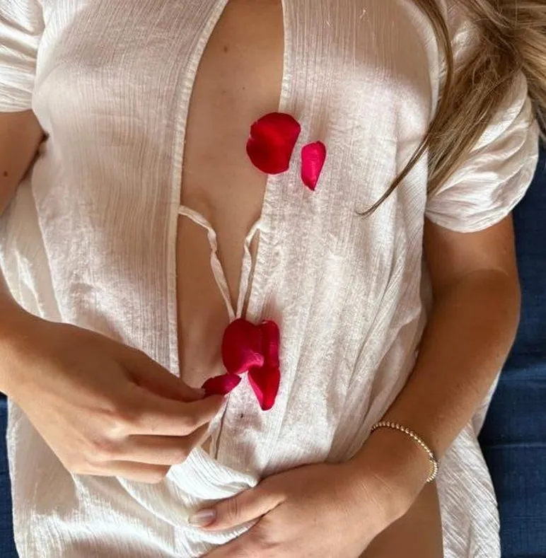 A woman resting in a white dress with rose petals on her body