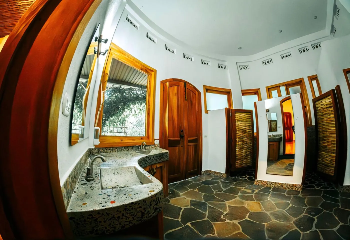 A stone-floored bathroom with a curved concrete double sink and wood cabinets