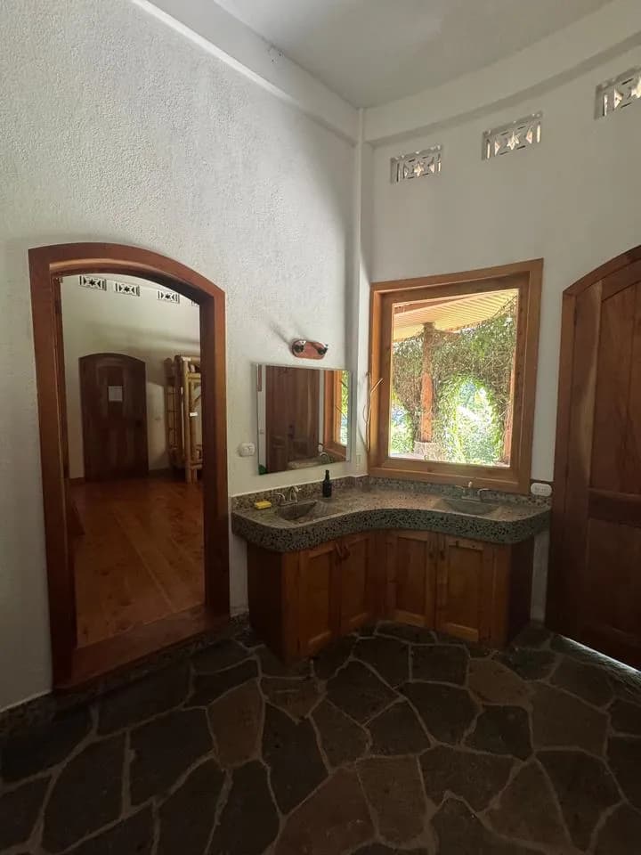 A bathroom sink with a mirror and a window onto green vines