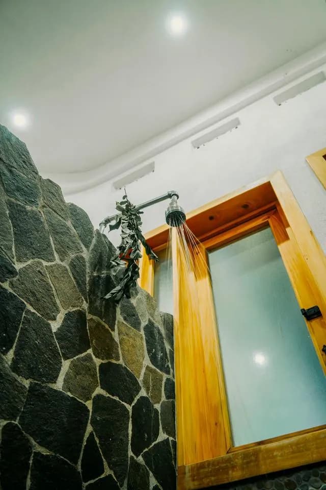 A stone shower with a rain shower head and a sprig of eucalyptus