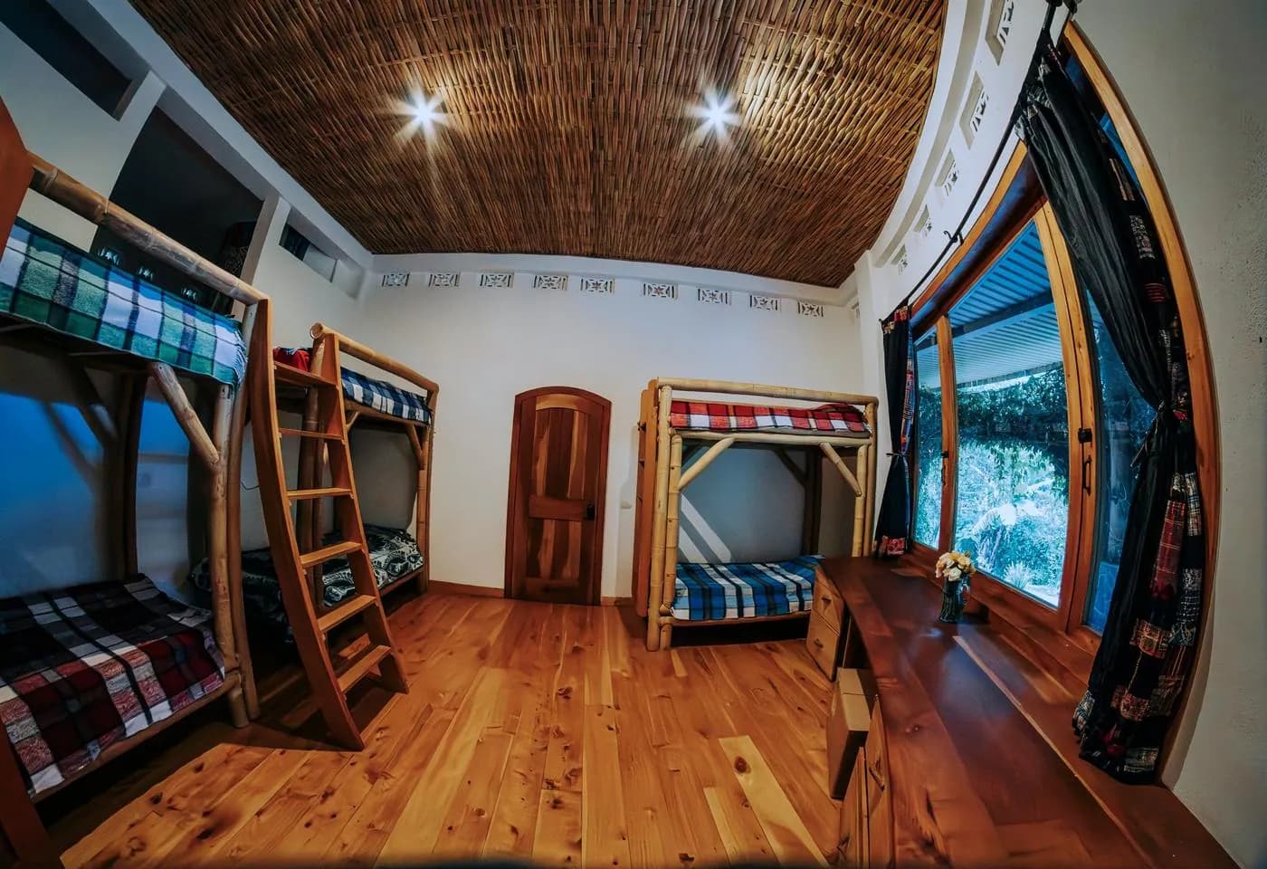 A bamboo bunk room with a woven reed ceiling and a big window onto the garden