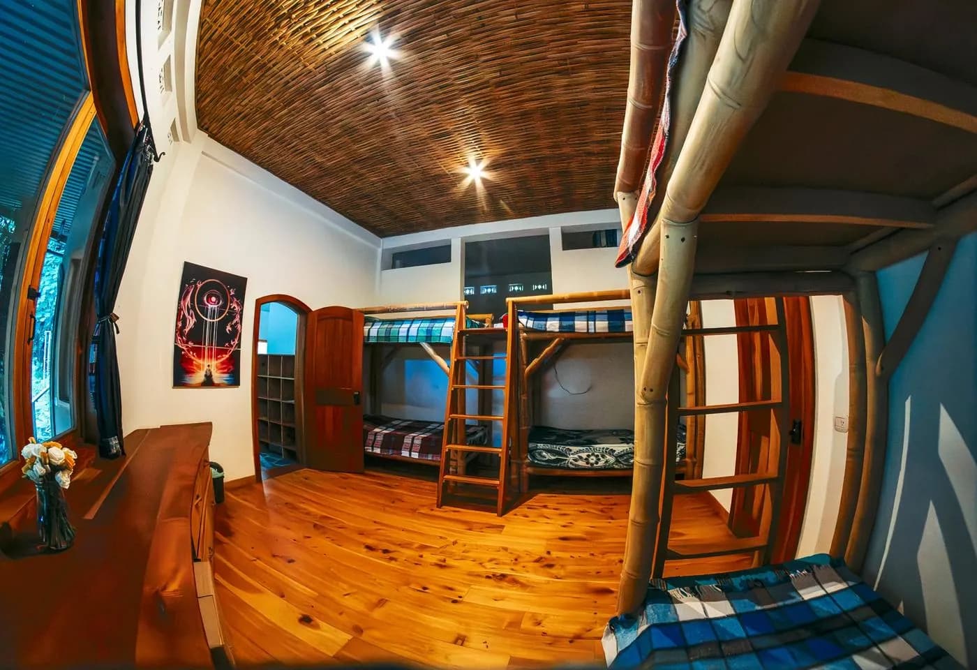 Bamboo bunk beds under a woven ceiling, with a painted poster and a long wooden desk