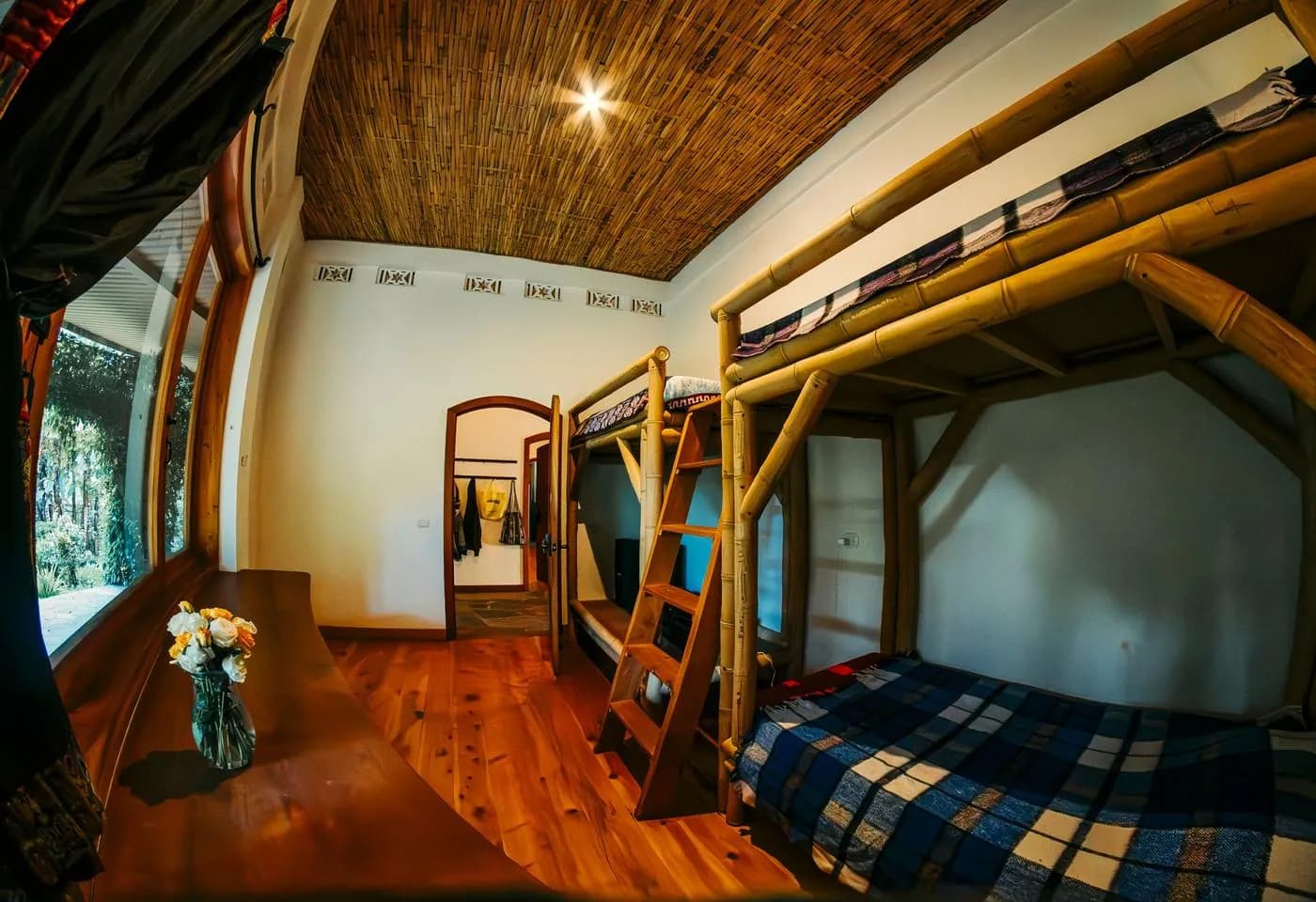 A bunk room with a vase of roses on a wooden desk by the window