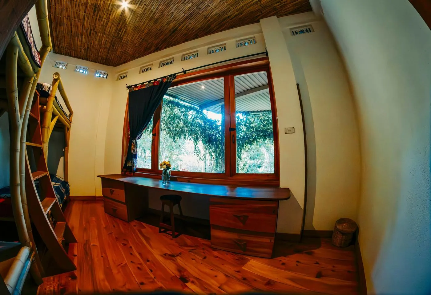 A wooden desk and stool under a large window with garden views