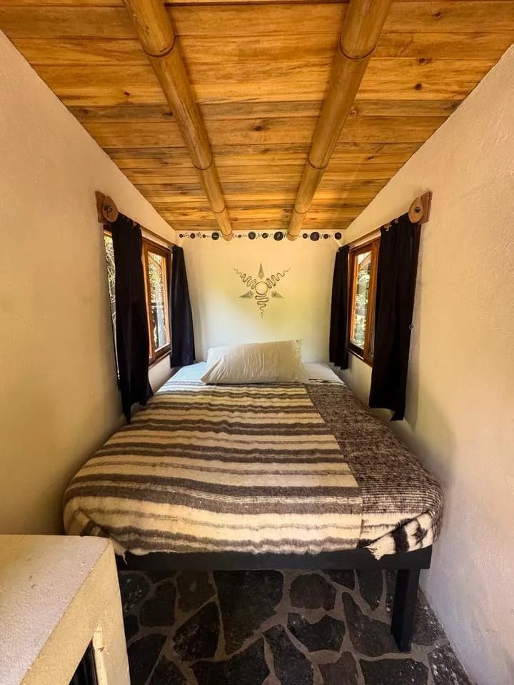 A cabin bed with a striped wool blanket, a bamboo-beam ceiling and a hand-painted sun on the wall