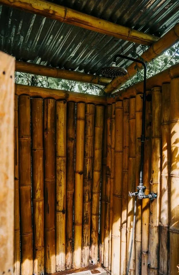 A bamboo outdoor shower with a rain shower head under a tin roof