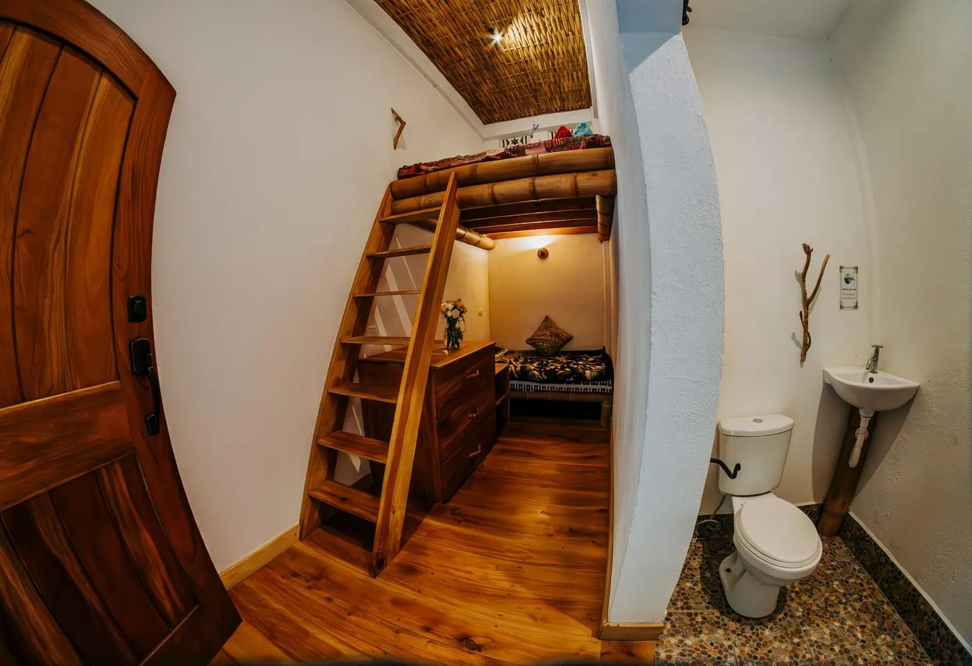 A private loft room with a wooden ladder, a bed beneath the loft, and a toilet and sink to the right