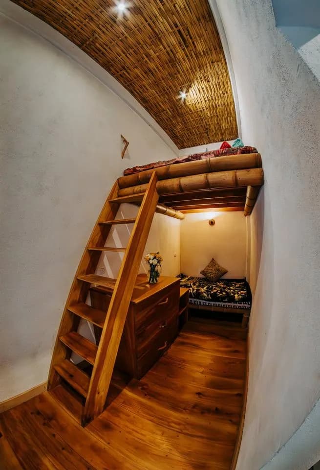 A loft bed above a daybed with a wooden dresser and a vase of flowers