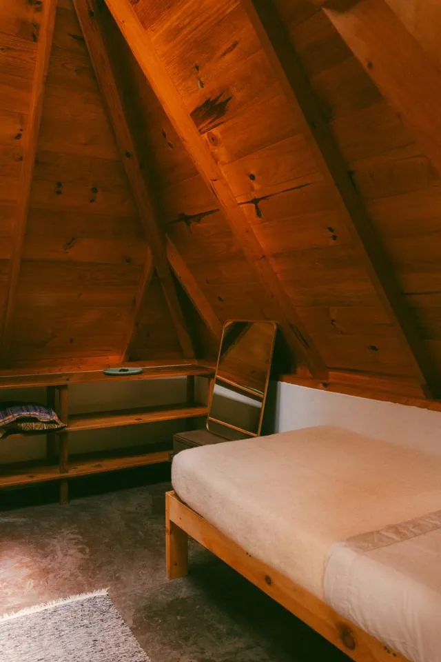 A twin bed with white linens under the wood-beamed pyramid ceiling