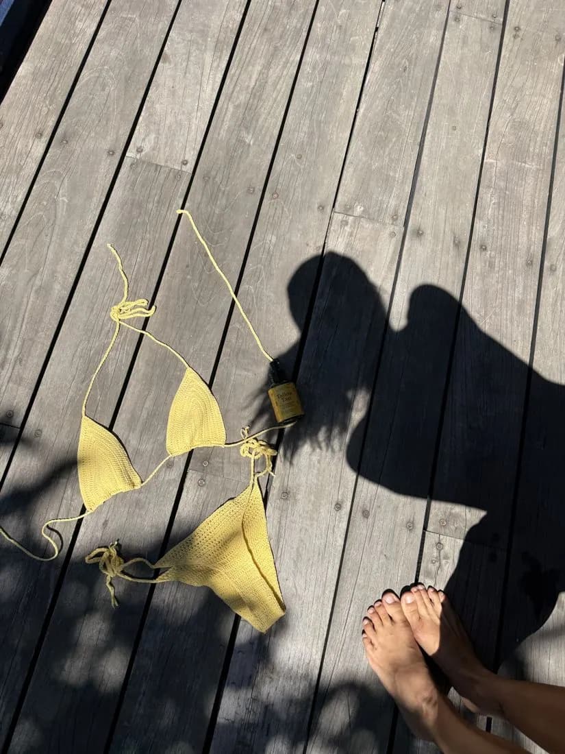 A yellow crochet bikini laid on a sunlit wooden deck