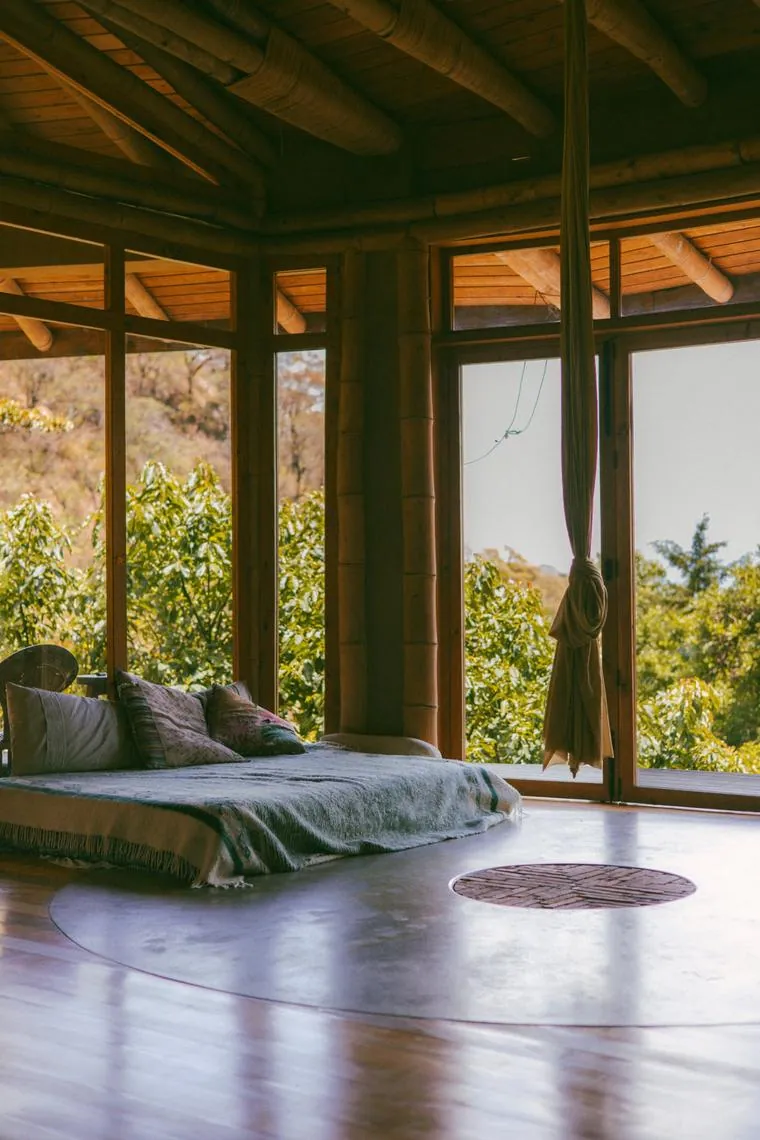 A light-filled wood and glass room with a floor bed and a round rug