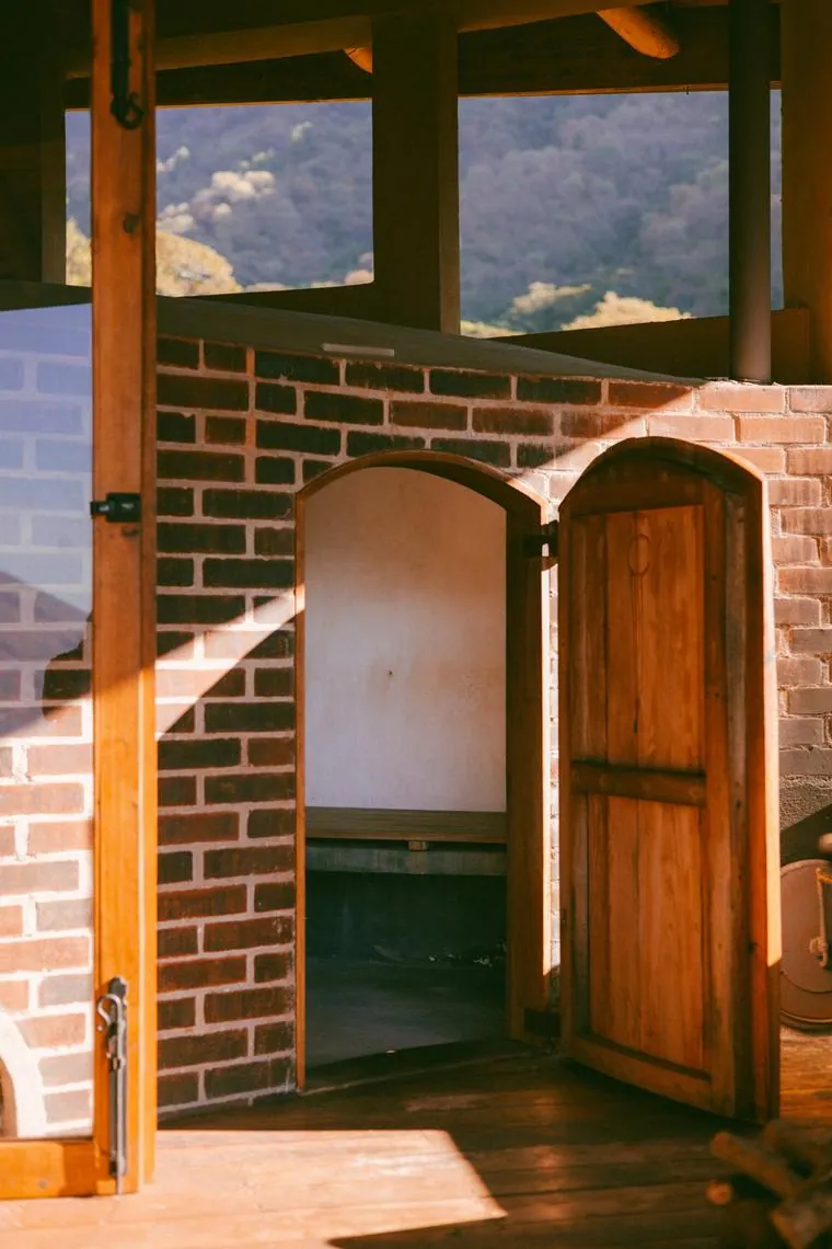 The brick sauna with an arched wooden door, open to the trees