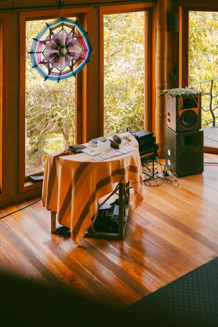 A table with sound equipment and a hanging mandala beside tall studio windows