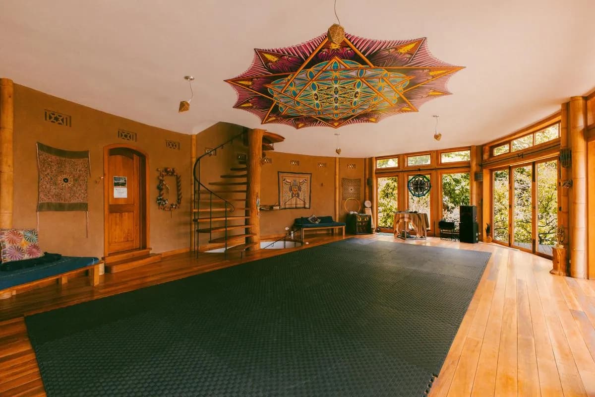 The wide wood and glass studio with a black yoga mat and a painted mandala ceiling