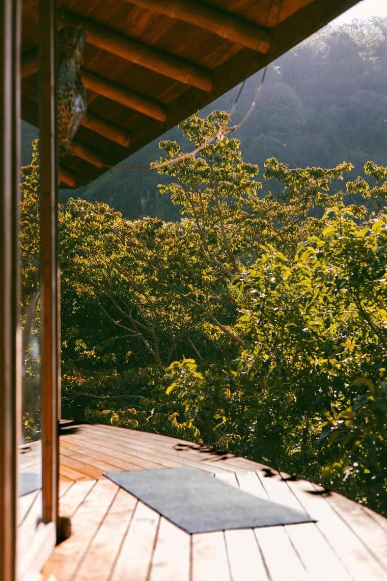 A wooden top deck with a yoga mat, looking out over the forest