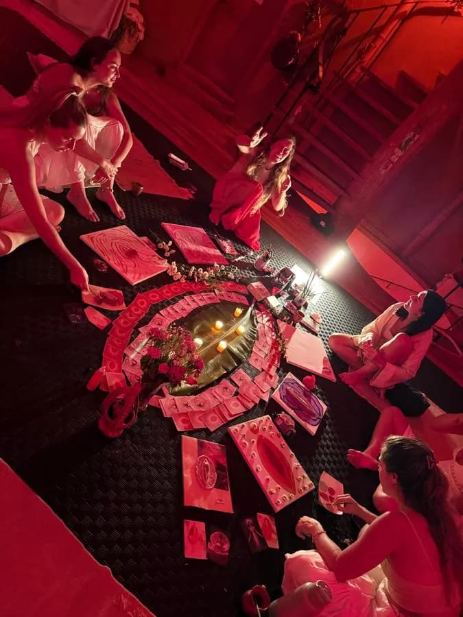 Women painting around a candlelit altar of flowers and cards in red light