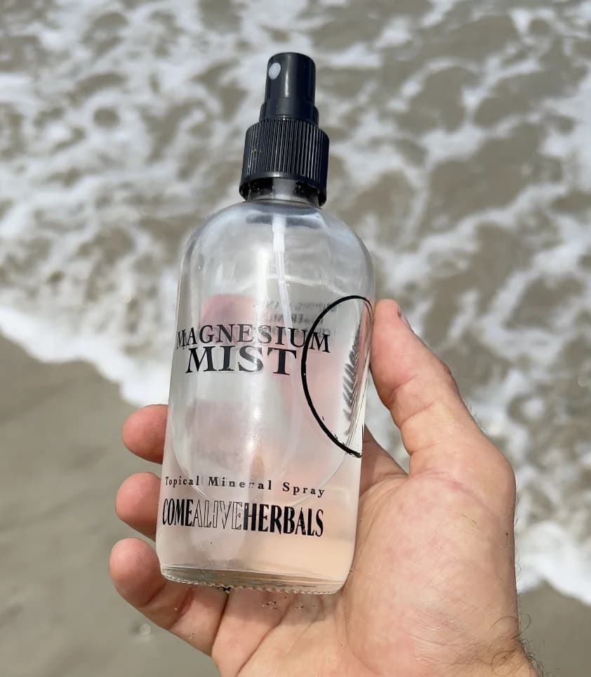 Come Alive Herbals bottle held above clear coastal water